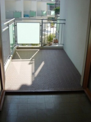 Ein Balkon mit Fliesenboden, Metallgeländer und Blick ins Freie.
