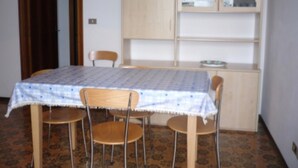 A room with a table, four chairs, a cabinet with glass doors, and patterned carpet. - Apartment 'Residence Torino 85' with Shared Pool and Private Terrace (Jesolo)