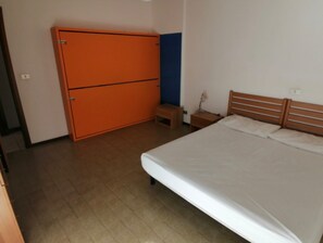 Een slaapkamer met een bed, een oranje garderobe, een houten nachtkastje en een klein tafeltje.
