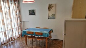 Zona de menjador amb taula i cadires, nevera, terra amb dibuixos i finestra amb cortines.