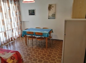 A dining area with a table and chairs, a refrigerator, patterned floor, and a window with curtains.