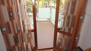 Una porta oberta que dona a un balcó amb paviment decorat, vista cap a l'exterior i una taula amb estovatge blau.