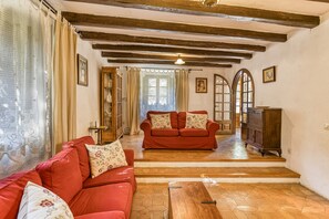 A room with two red sofas, wooden flooring, a wooden cabinet, and a staircase leading to another room.