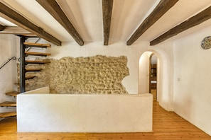 A staircase with a stone wall, wooden beams, and a white wall with a decorative plate.