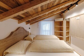 Ein Schlafzimmer mit Holzboden, einem Bett mit gestreifter Bettwäsche, einem Kopfteil und einem Fenster mit Vorhängen.