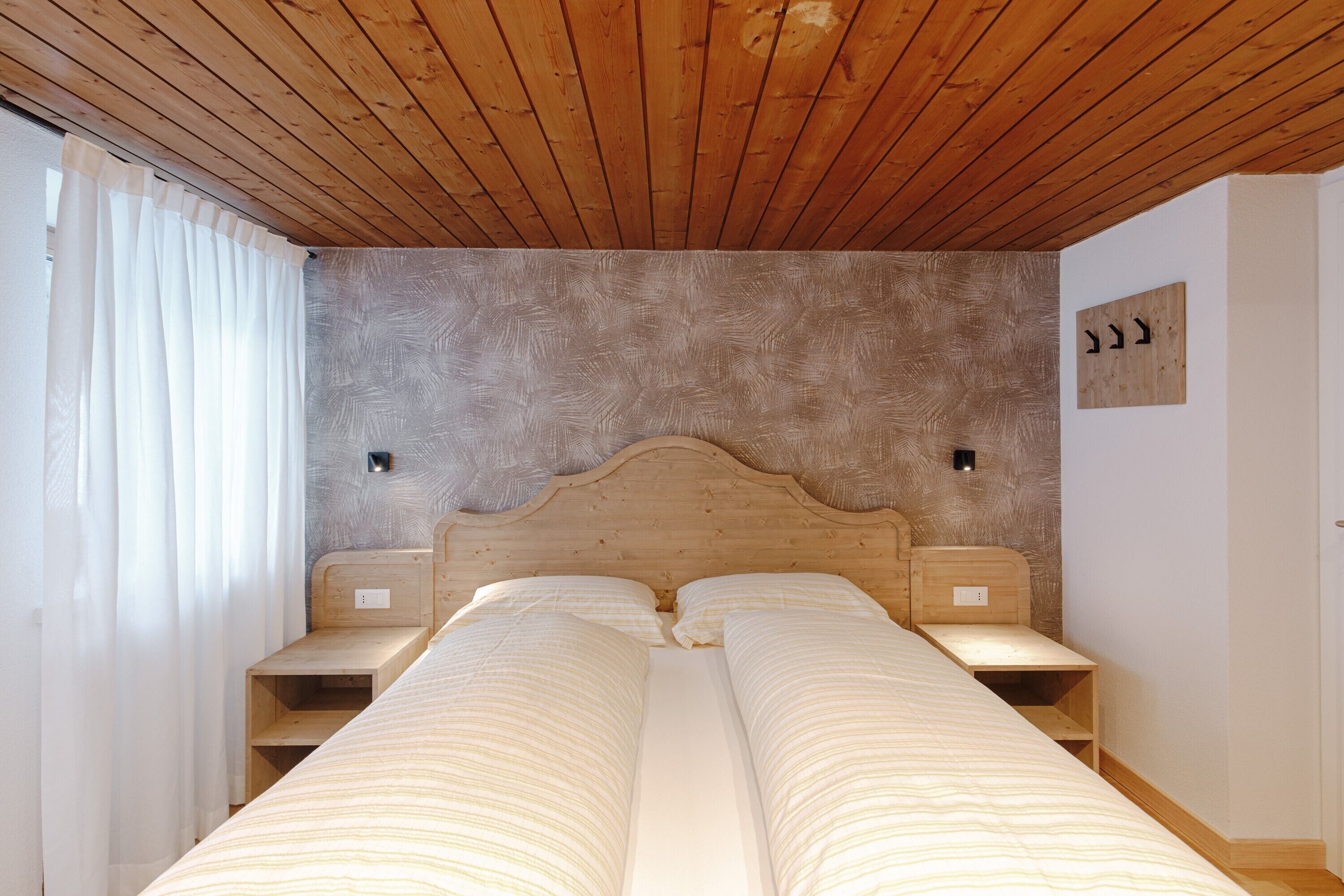 Ein Schlafzimmer mit Holzbalkendecke, einem Bett mit weißer Bettwäsche, zwei Nachttischen und einer wandmontierten Leuchte.