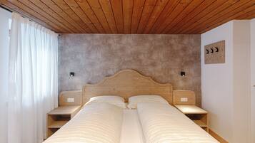 Ein Schlafzimmer mit Holzbalkendecke, einem Bett mit weißer Bettwäsche, zwei Nachttischen und einer wandmontierten Leuchte.