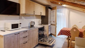 Cocina compacta con armarios de madera, microondas, lavavajillas y comedor con mesa y sillas.