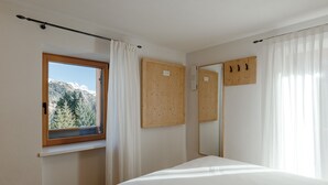 Makuuhuoneessa on sänky, ikkunassa verhot, puinen ovi ja peili seinällä.