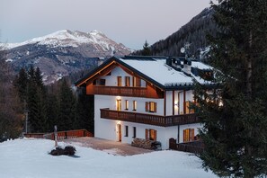 Un chalet à deux étages doté d’un balcon, d’une terrasse en bois et offrant une vue sur les montagnes.