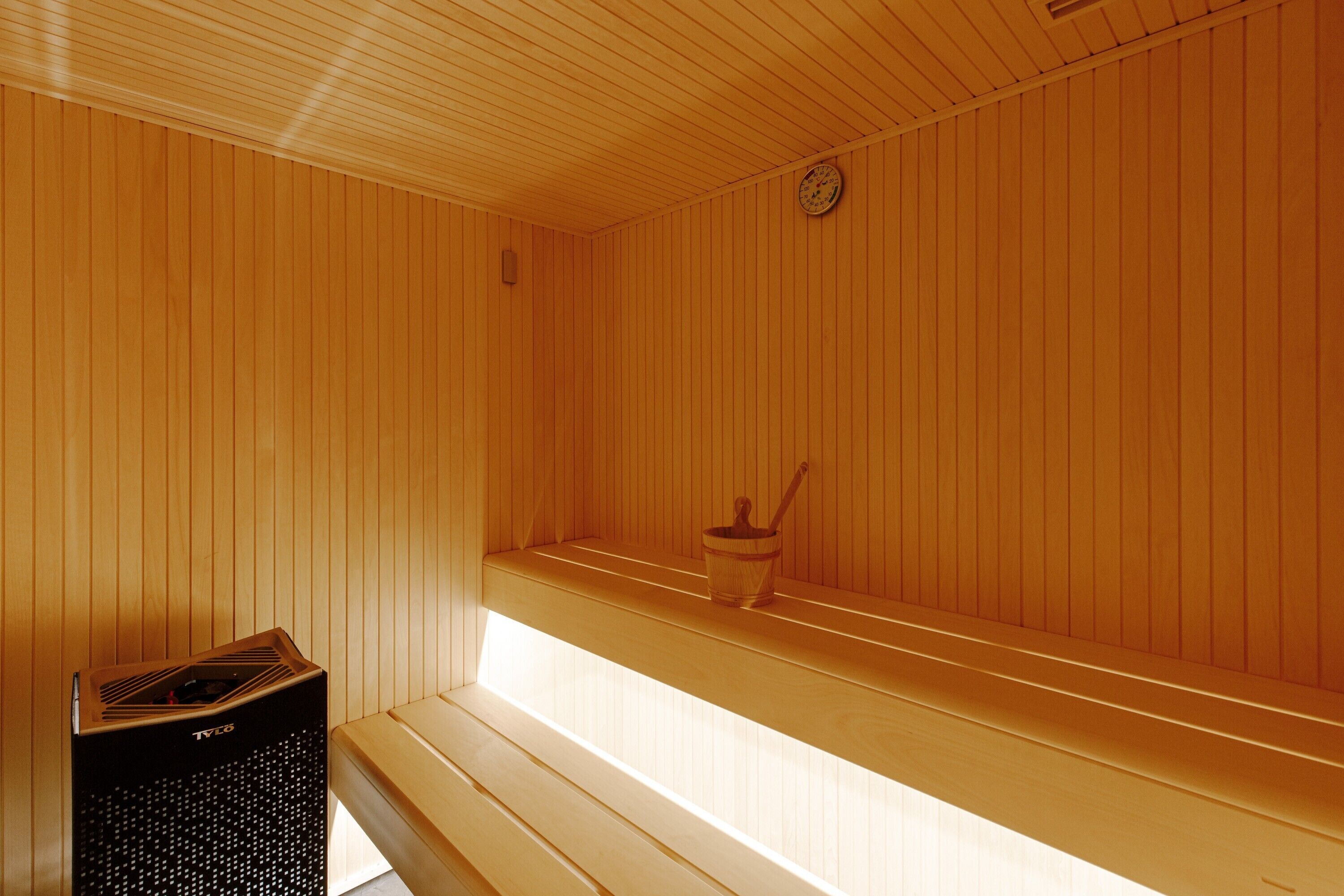 A sauna with wooden walls, a bench, a bucket, and a heater.