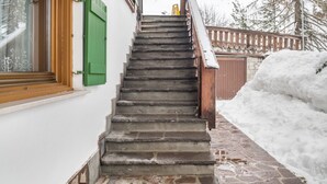 A staircase leading to a wooden door, a window with green shutters, and a snow-covered area.