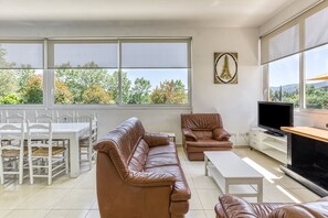 A living room with a sofa, TV, and dining area with chairs and a table. - Holiday Home 'Usall Rural' with Private Pool, Wi-Fi and Air Conditioning (Porqueres)