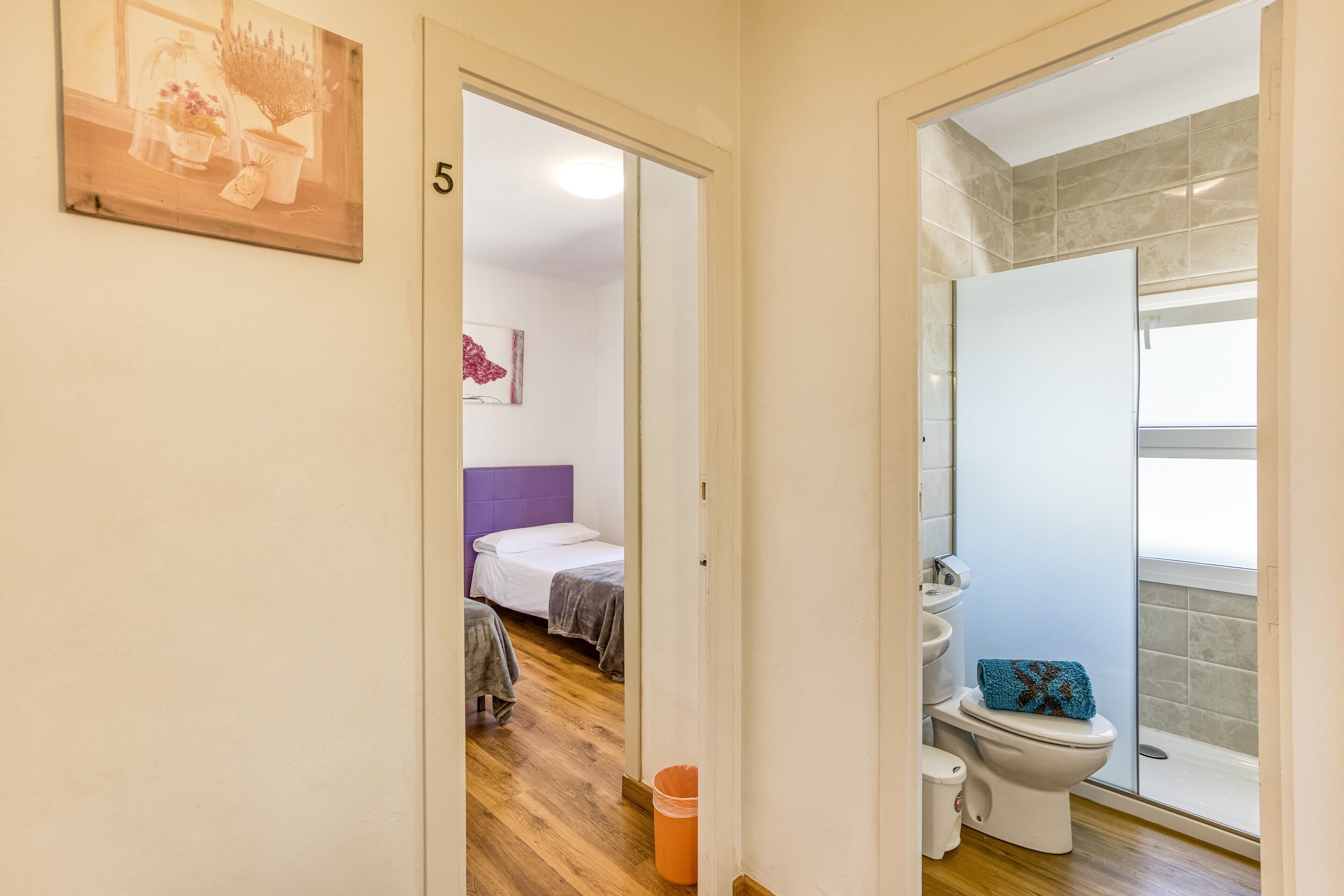 A hallway leading to a bedroom with a bed, a bathroom with a toilet and shower, and a number '5' on the wall.