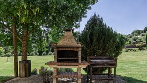 An outdoor brick oven with a chimney, a grill, and a wooden table, surrounded by trees and a grassy field. - Holiday Home 'Usall Rural' with Private Pool, Wi-Fi and Air Conditioning (Porqueres)