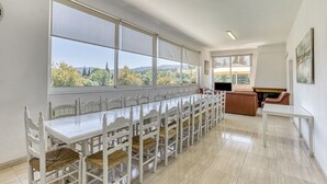 A dining area with a long table and chairs, large windows with a view, and a separate seating area with a couch and table. - Holiday Home 'Usall Rural' with Private Pool, Wi-Fi and Air Conditioning (Porqueres)