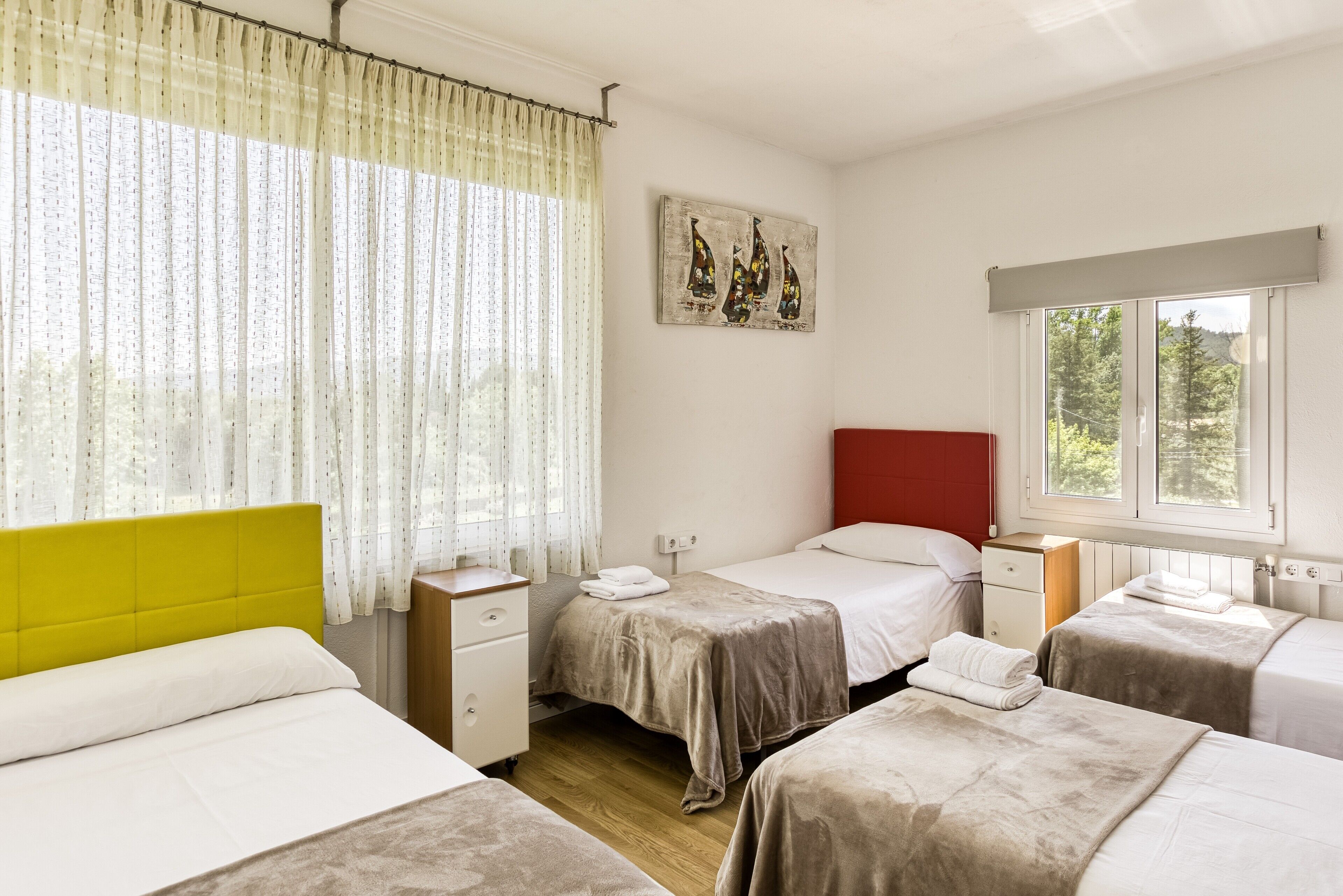 Une chambre d’hôtel avec deux lits, une fenêtre donnant sur un paysage agréable, un tableau au mur et un rideau.