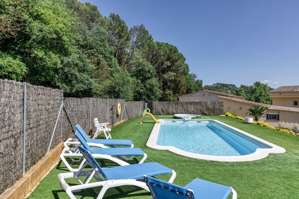 A swimming pool with blue and white lounge chairs, a hot tub, and a wooden deck.