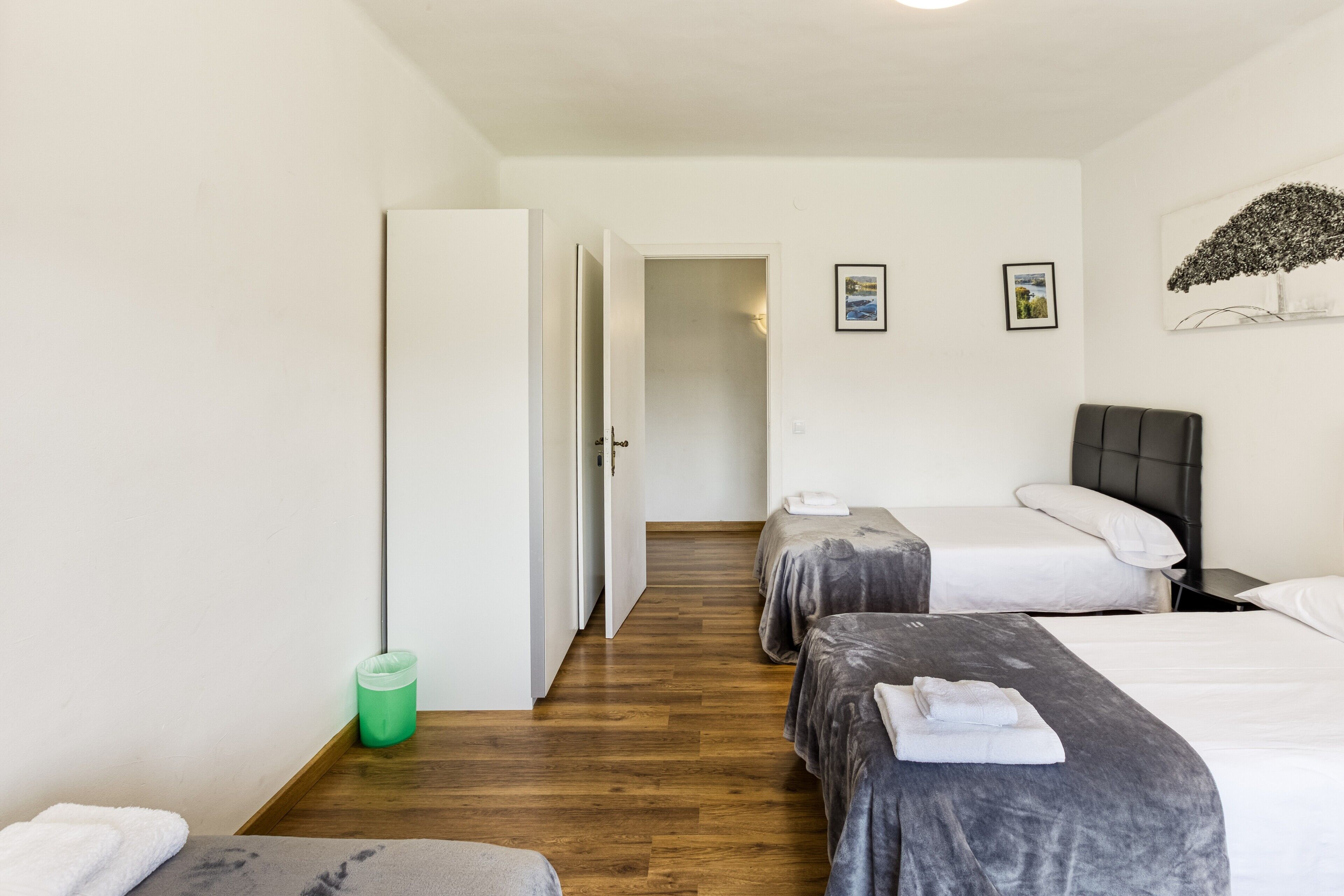 Une chambre d’hôtel avec deux lits, une poubelle verte, un plancher en bois et une porte donnant sur une autre pièce.