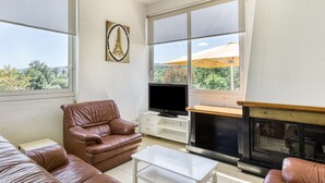 A living room with a leather sofa, a television, a fireplace, and a large window with a view of trees. - Holiday Home 'Usall Rural' with Private Pool, Wi-Fi and Air Conditioning (Porqueres)