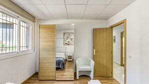 A hotel room with a wooden floor, a bed, a chair, a mirror, and a view through a window. - Holiday Home 'Usall Rural' with Private Pool, Wi-Fi and Air Conditioning (Porqueres)