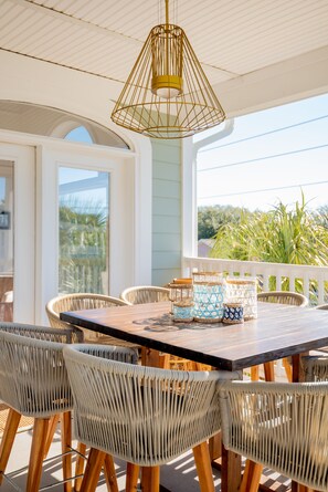 A covered patio with a wooden table and wicker chairs, featuring a gold pendant light and decorative jars. - IDEAL IOP Beach Home, 6 BR, Private Pool, Close to Beach, Spacious! (Isle Of Palms)