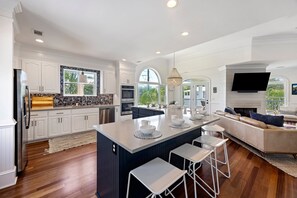 A modern kitchen with white cabinetry, a central island, and a dining area with a sofa and chairs. - IDEAL IOP Beach Home, 6 BR, Private Pool, Close to Beach, Spacious! (Isle Of Palms)