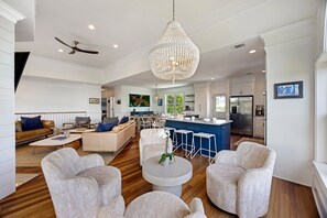 A spacious living area with a large chandelier, a kitchen with a blue island, and a dining area with bar stools. - IDEAL IOP Beach Home, 6 BR, Private Pool, Close to Beach, Spacious! (Isle Of Palms)
