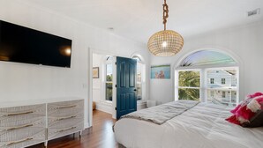Une chambre à coucher avec un grand lit, un téléviseur fixé au mur et une vue sur l’extérieur par une fenêtre.