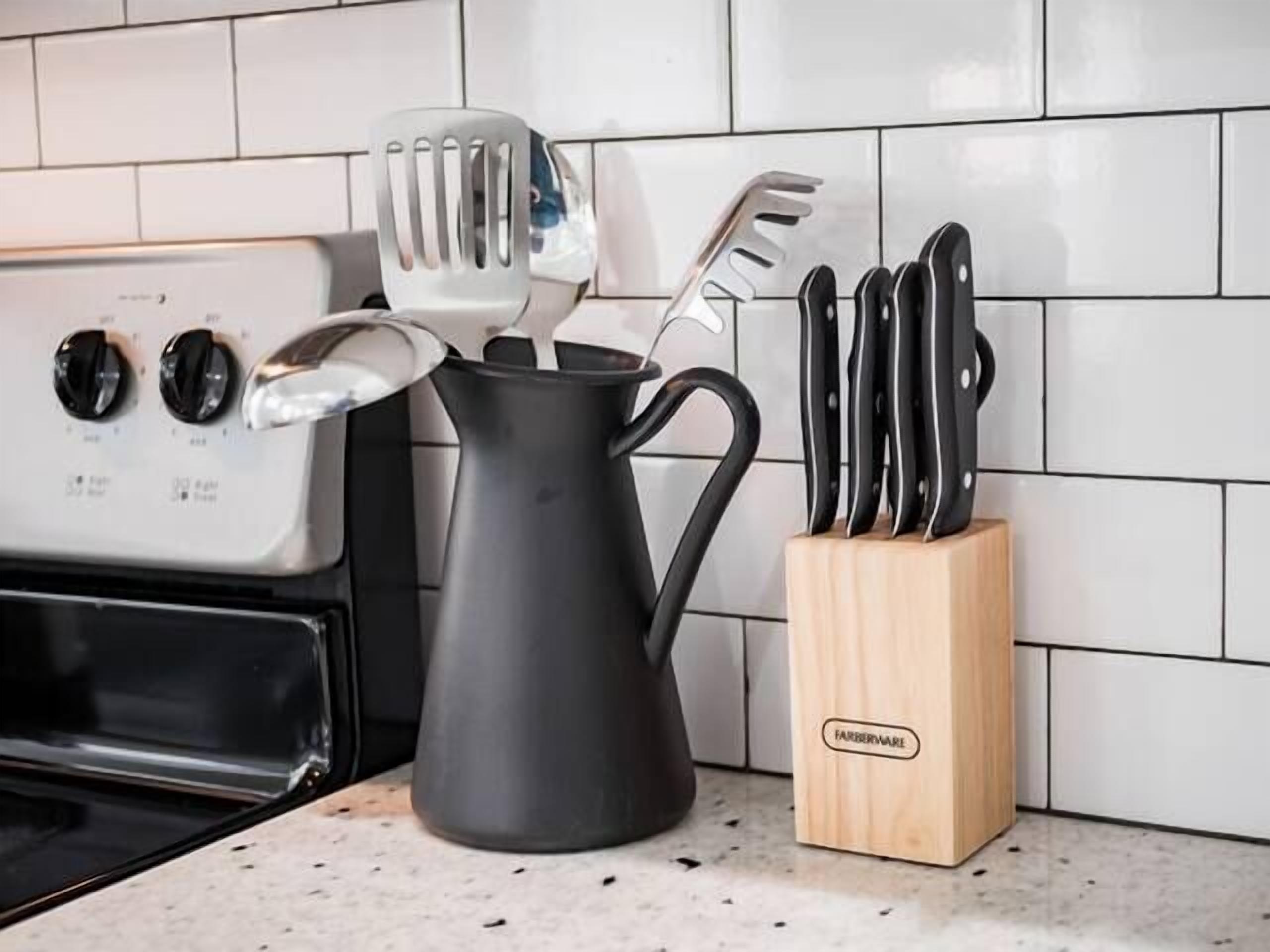 A kitchen with a black kettle, a wooden knife block, and a white tiled backsplash.