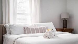 A neatly made bed with white linens, a striped pillow, and rolled towels on a wooden nightstand. - Gorgeous Getaway -1BR- Columbus! (Columbus)