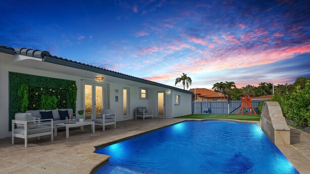 Una piscina con zona de patio, mobiliario exterior y un cielo al atardecer.