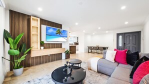 Una sala de estar moderna con un televisor de pantalla plana, un sofá gris con cojines rojos y negros, una mesa de centro negra y un aparador de madera.