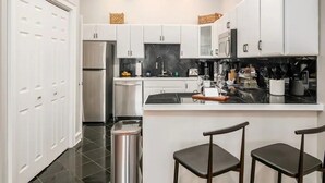 Una cocina moderna con armarios blancos, un refrigerador de acero inoxidable y una encimera negra.