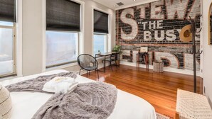A modern bedroom with a large bed, a fireplace, and a wall with the text "STEW THE BUS." - THE SKYSCRAPER IN HEART OF COLUMBUS (Columbus)