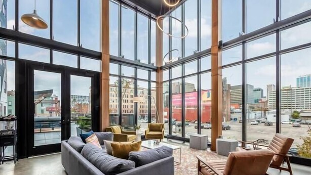 A spacious lobby with large windows, a grey sofa, wooden chairs, and a coffee table. - Shades of Blue Elegant Suite l Free Parking + Gym (Columbus)
