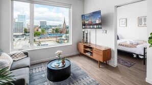 A modern living room with a large window, a flat-screen TV, a sofa, a coffee table, and a bed. - Shades of Blue Elegant Suite l Free Parking + Gym (Columbus)