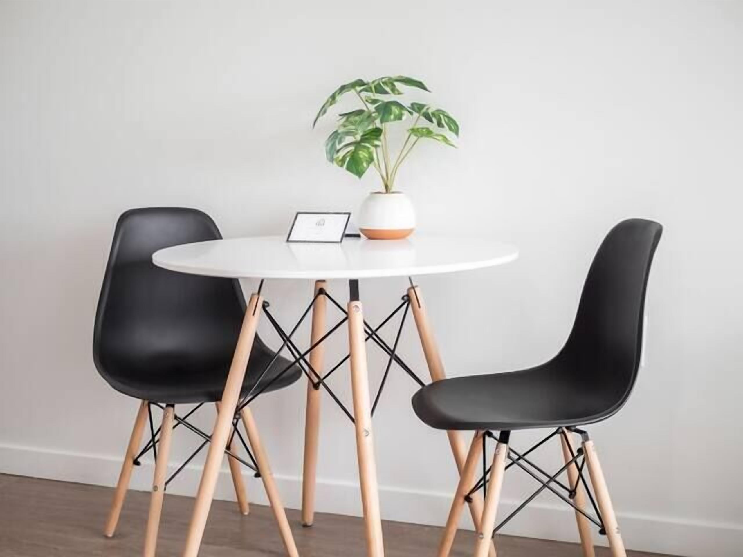 Un espace repas moderne avec une table ronde blanche, deux chaises noires et une plante en pot.