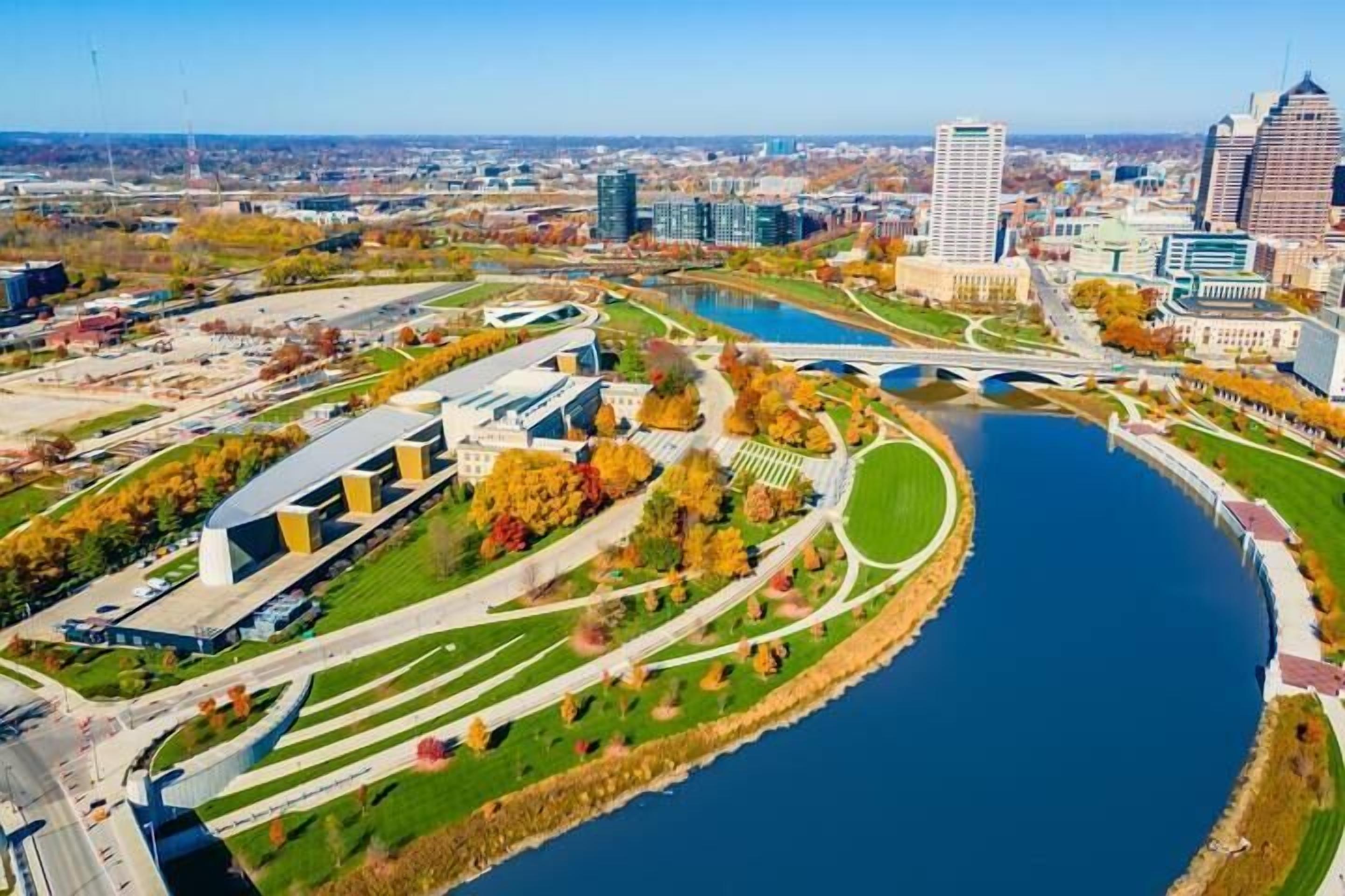 An aerial view of a cityscape with a river, modern buildings, and a bridge.