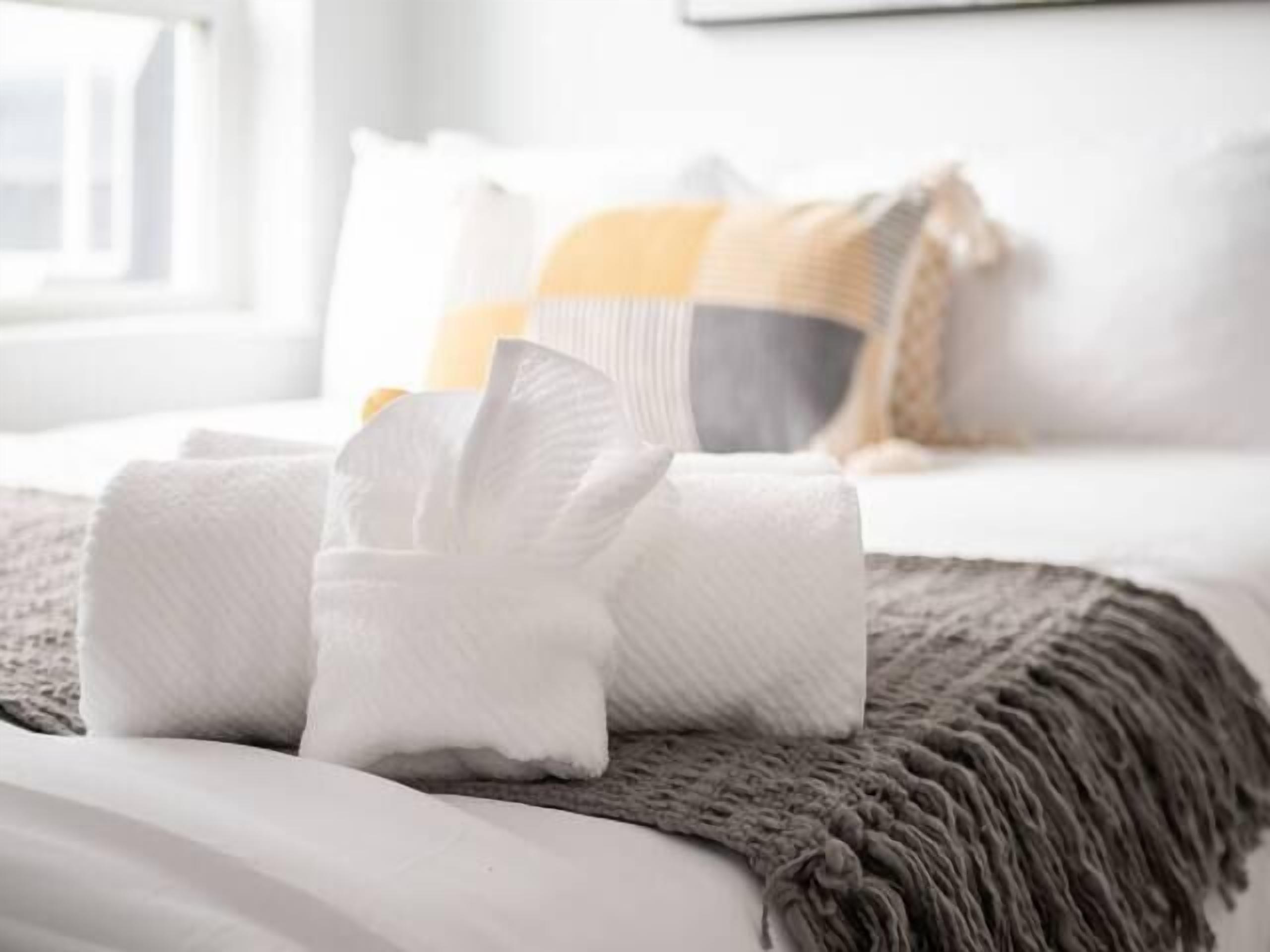 A neatly made bed with a rolled white towel and a gray knitted blanket.