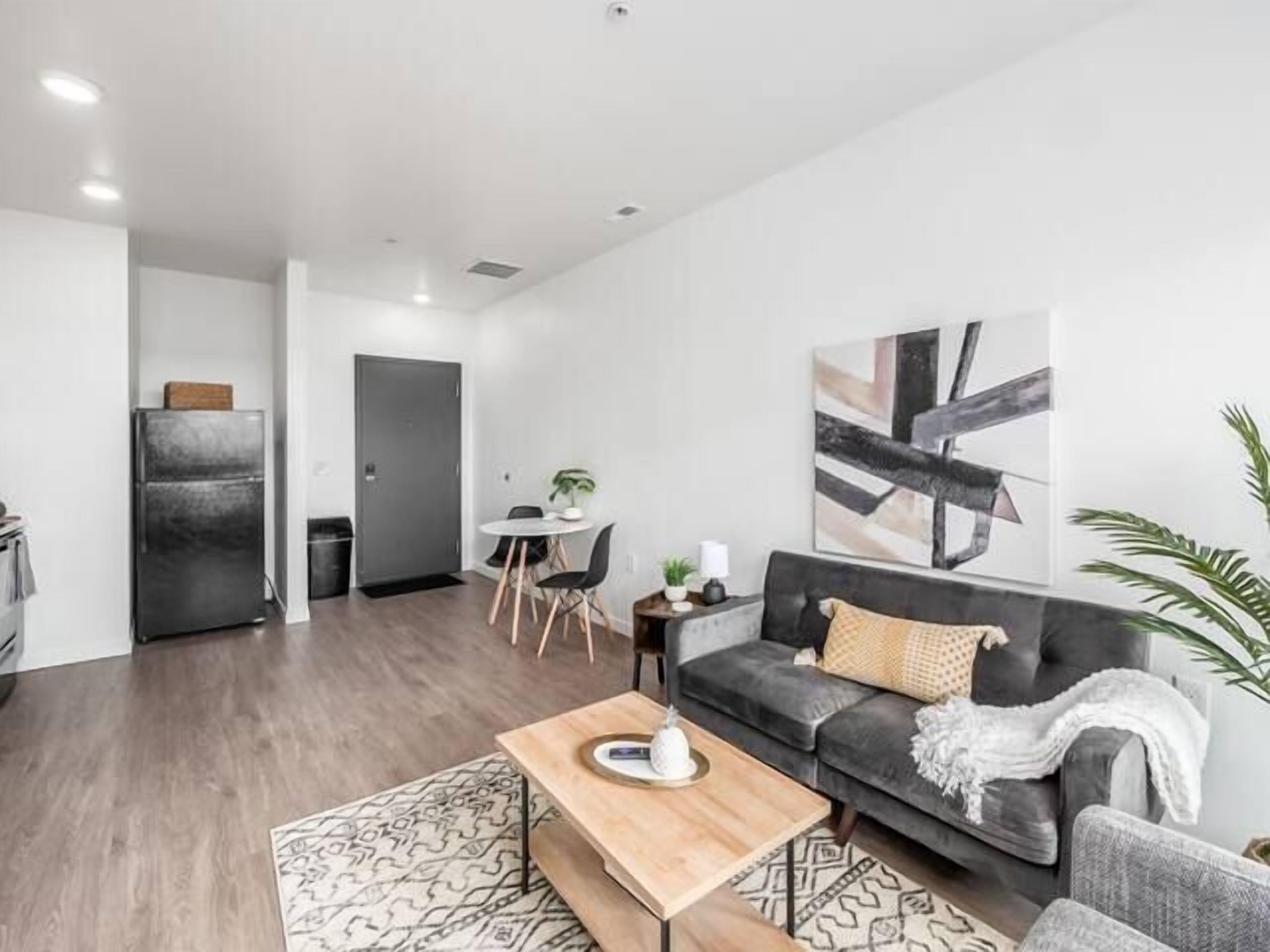 Uma sala de estar moderna com um sofá cinzento, uma mesa de centro de madeira e um tapete estampado.