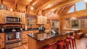 Ein Holzblockhaus-Interieur mit einer Küche, die eine große Kochinsel, Barhocker und einen Esstisch umfasst.