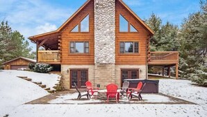 Eine Blockhütte mit einem Steinsschornstein, einer Holzterrasse und einer Sitzgelegenheit im Freien.