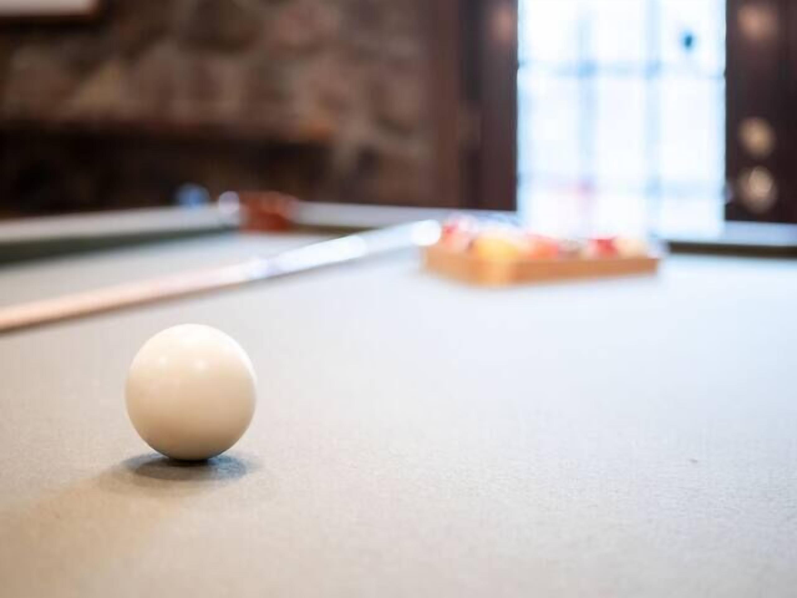 A billiards table with a white cue ball in focus and a striped cushion in the background.