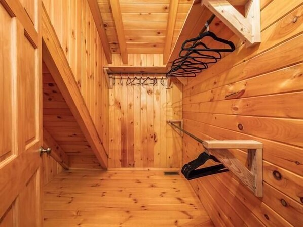 Interior de madera con techo inclinado, un perchero metálico y una pequeña estantería.