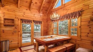 Ein Holzblockhaus-Interieur mit Esstisch, Bänken, einer Chandeliebre und großen Fenstern.