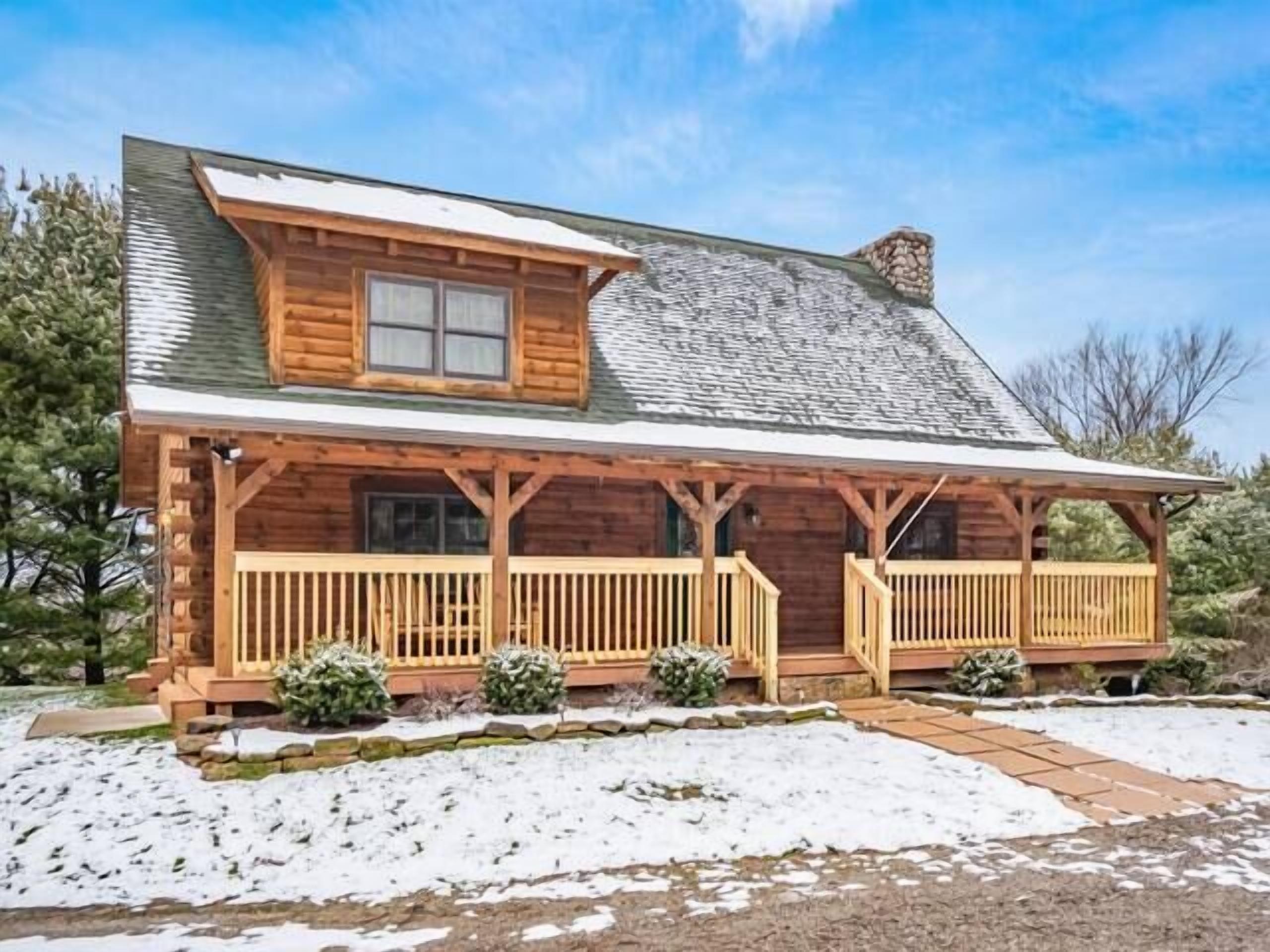 A log cabin with a porch, a chimney, and a snow-covered landscape.