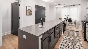 A modern kitchen with a central island, dark cabinets, and a patterned rug. - Oak Street Rooftop - Columbus! (Columbus)