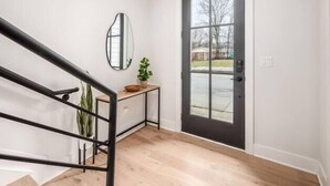 A modern interior with a staircase, a door with a glass panel, a small table with a plant, and a wall-mounted mirror. - Oak Street Rooftop - Columbus! (Columbus)