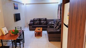A compact living space with a dining area, a sofa set, a flat-screen TV, and a water dispenser.